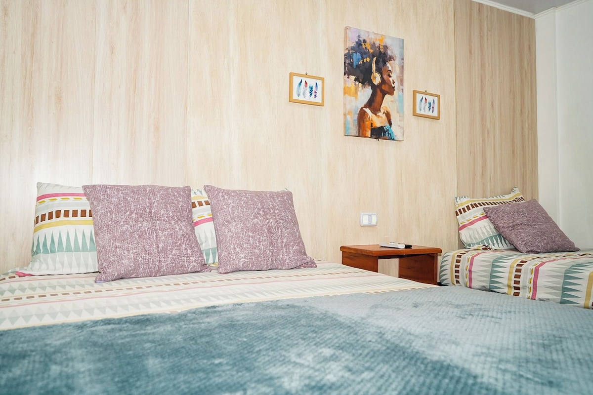 A hotel room with a bed, pillows, a nightstand, and two wall-mounted paintings.