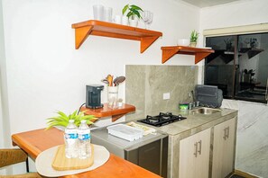 A compact kitchen with a coffee maker, a sink, and a stove. There are wooden shelves above the counter and a potted plant on the counter. - Posada Kotnat (San Andrés Isla, San Luis)