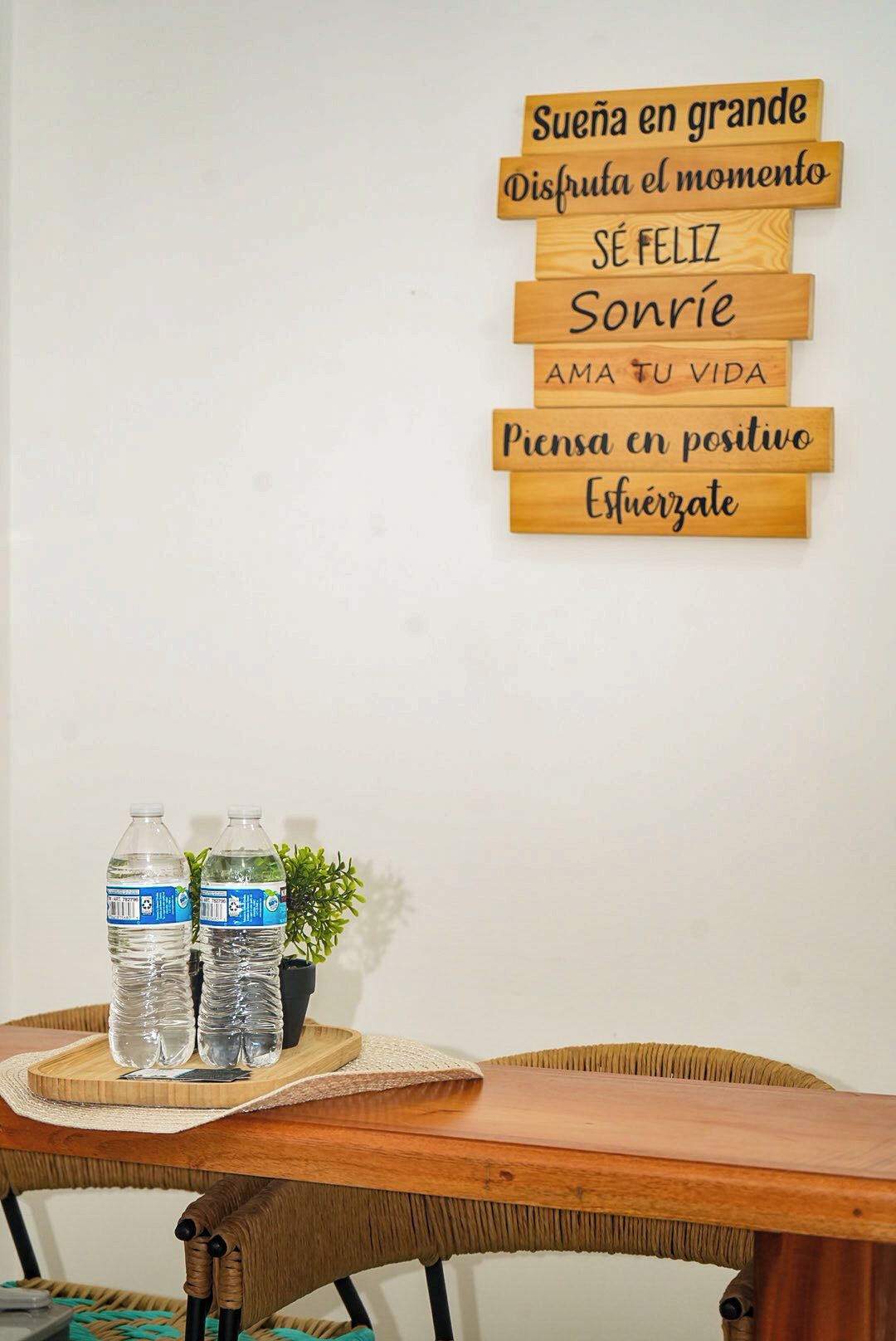 Una pared con placas de madera con mensajes motivacionales y dos botellas de agua sobre una mesa con una silla de mimbre.