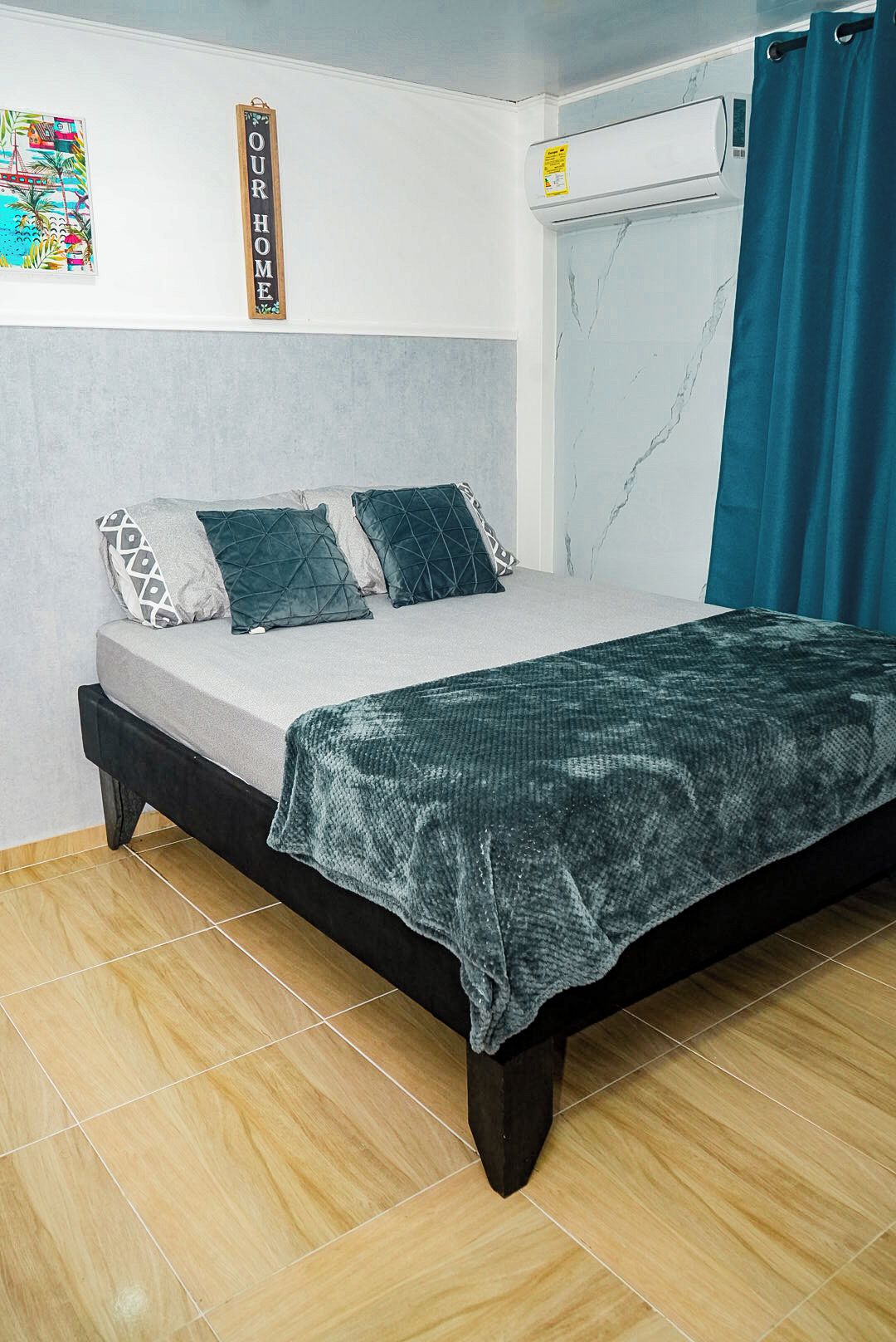 A bedroom with a bed, pillows, a wall-mounted air conditioner, and a curtain.