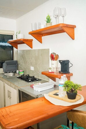 Una cocina moderna con estantes de madera, estufa a gas, lavamanos y una zona de comedor con una silla.