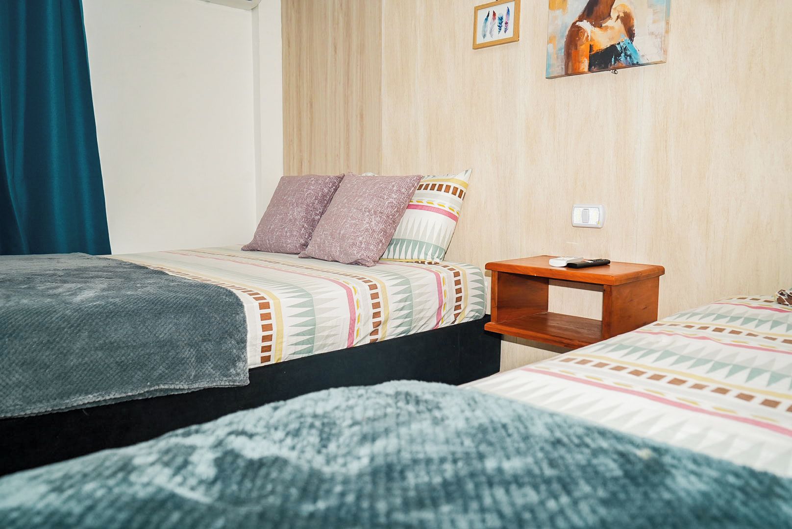 Une chambre avec deux lits, une table de chevet et un interrupteur fixé au mur.