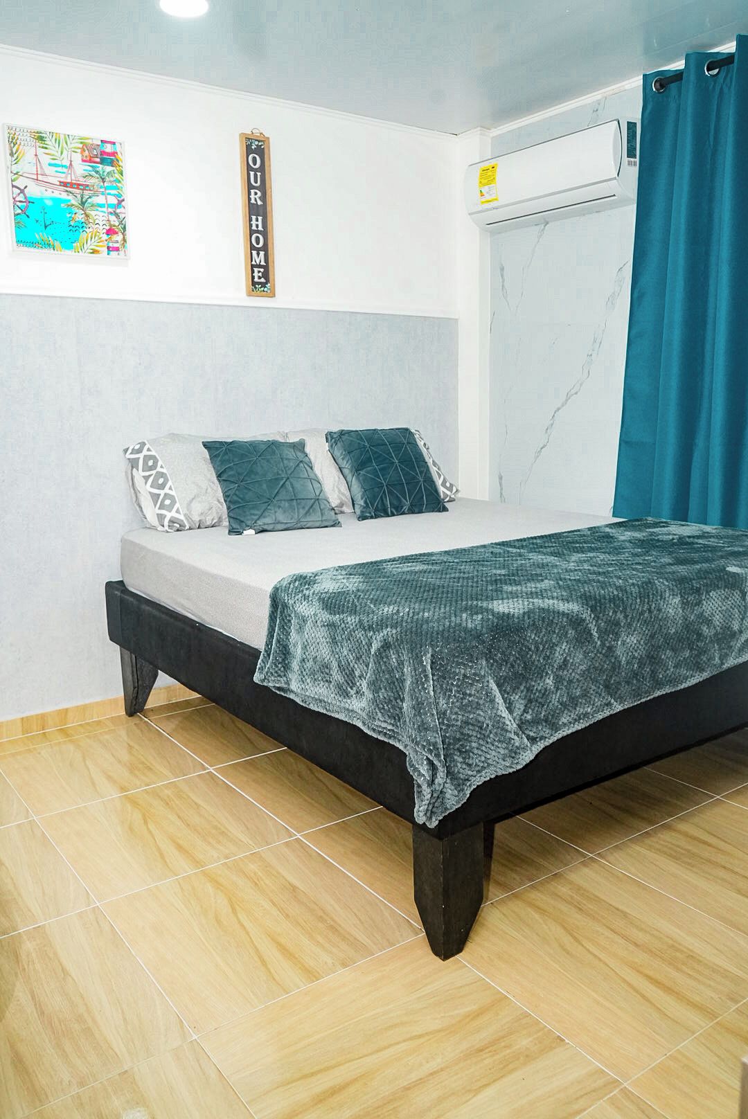 Un dormitorio con cama, almohadas, aire acondicionado de pared y ventana con cortina.