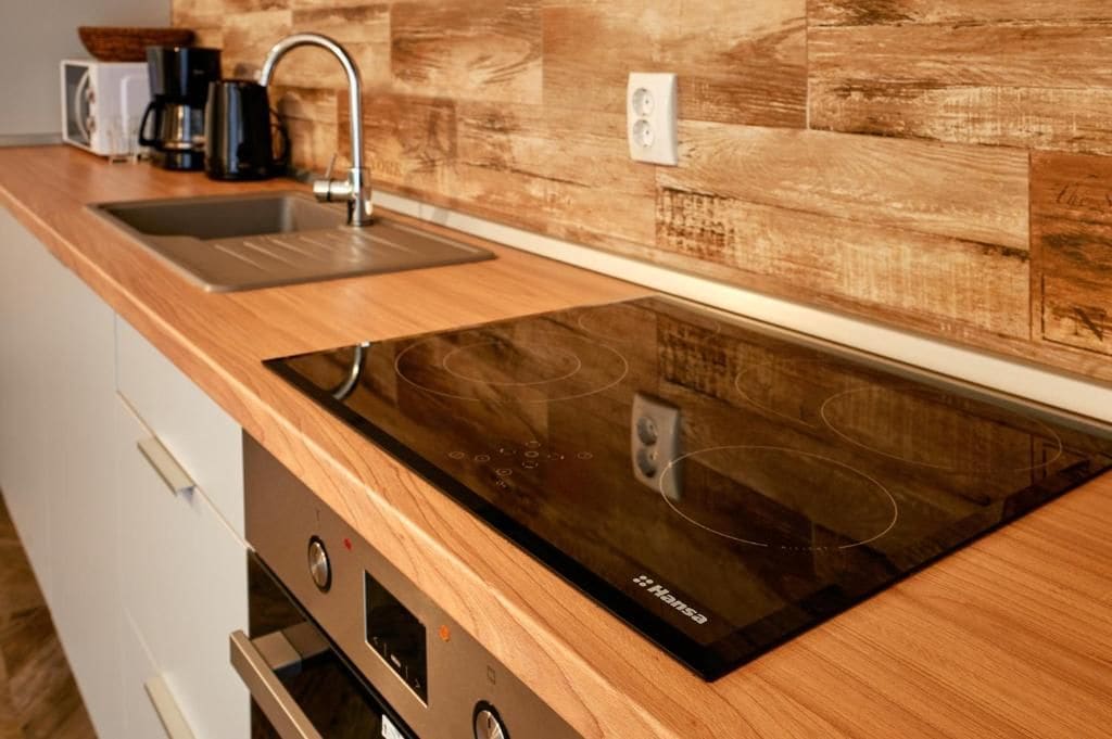 Une cuisine dotée d’une plaque de cuisson à induction intégrée, d’un évier en acier inoxydable et d’un crédence en bois.