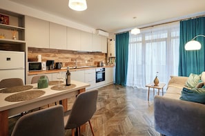 A modern kitchen with a dining area, a sofa, and a small table with a vase. - NUUC Aparthotel (Cluj-Napoca)