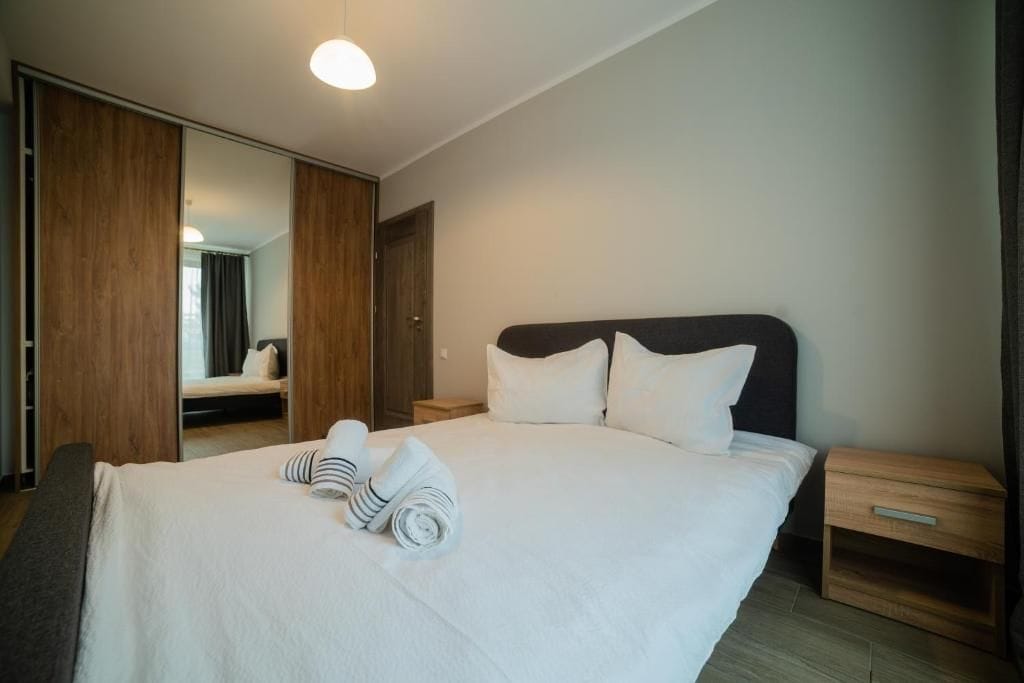 A hotel room with a large bed, a wooden wardrobe, a bedside table, and a mirror.