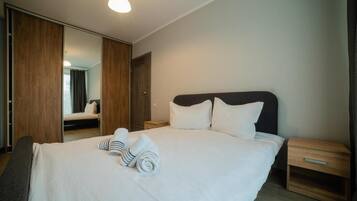 A hotel room with a large bed, a wooden wardrobe, a bedside table, and a mirror.
