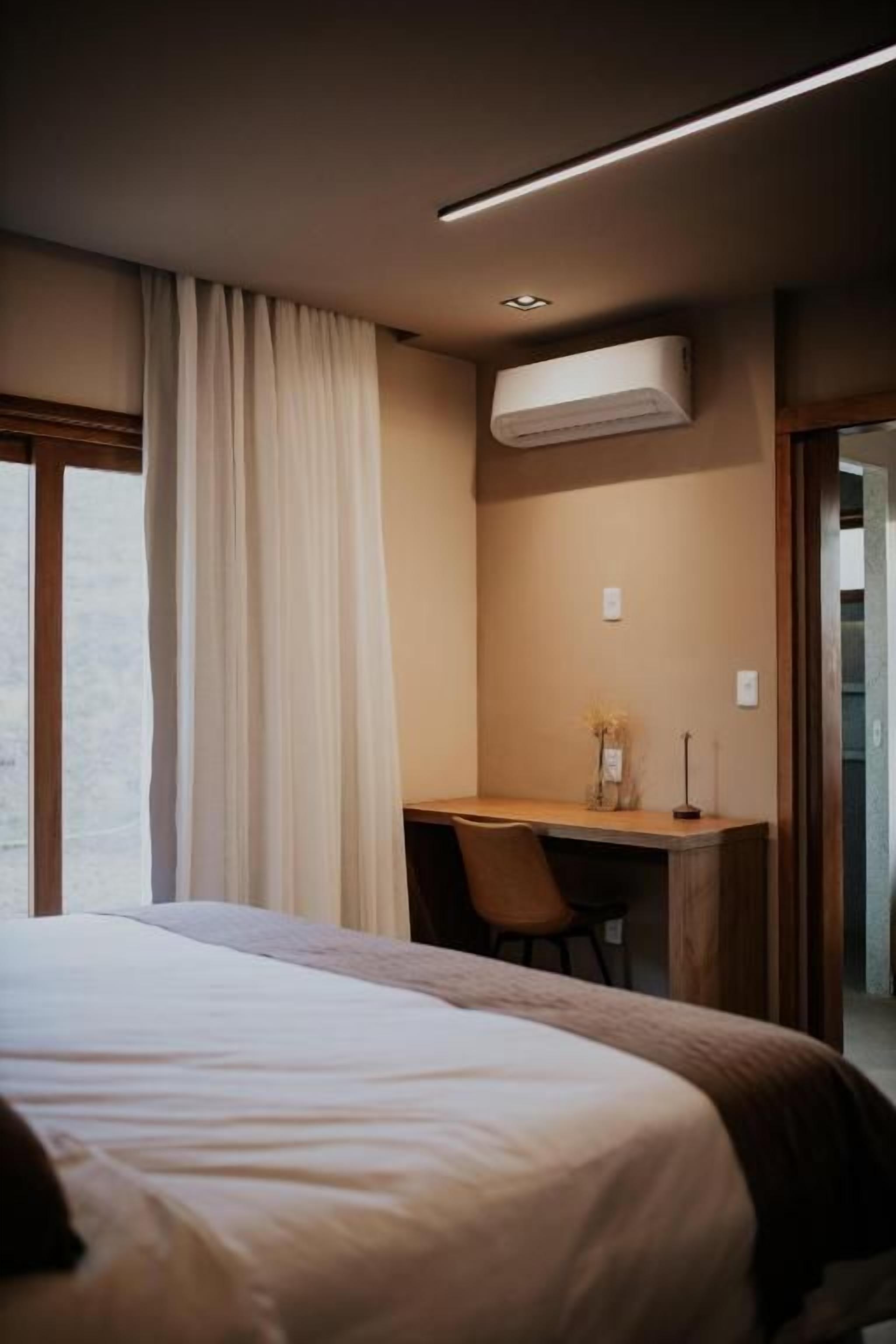 A hotel room with a bed, a desk, and an air conditioning unit.