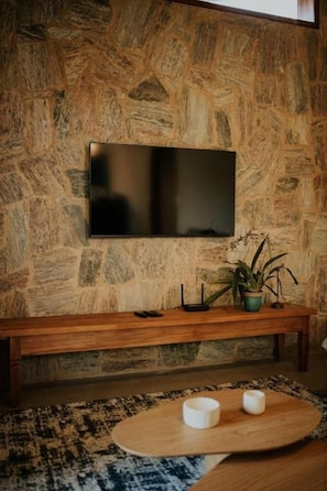 A stone wall with a flat-screen TV mounted above a wooden bench. - Villa Arouca (Areal)