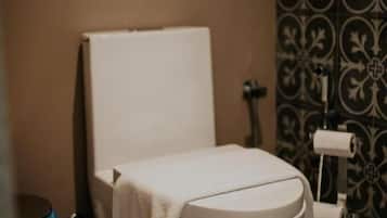 A standard toilet with a towel on the seat, a toilet paper holder, and a trash bin.