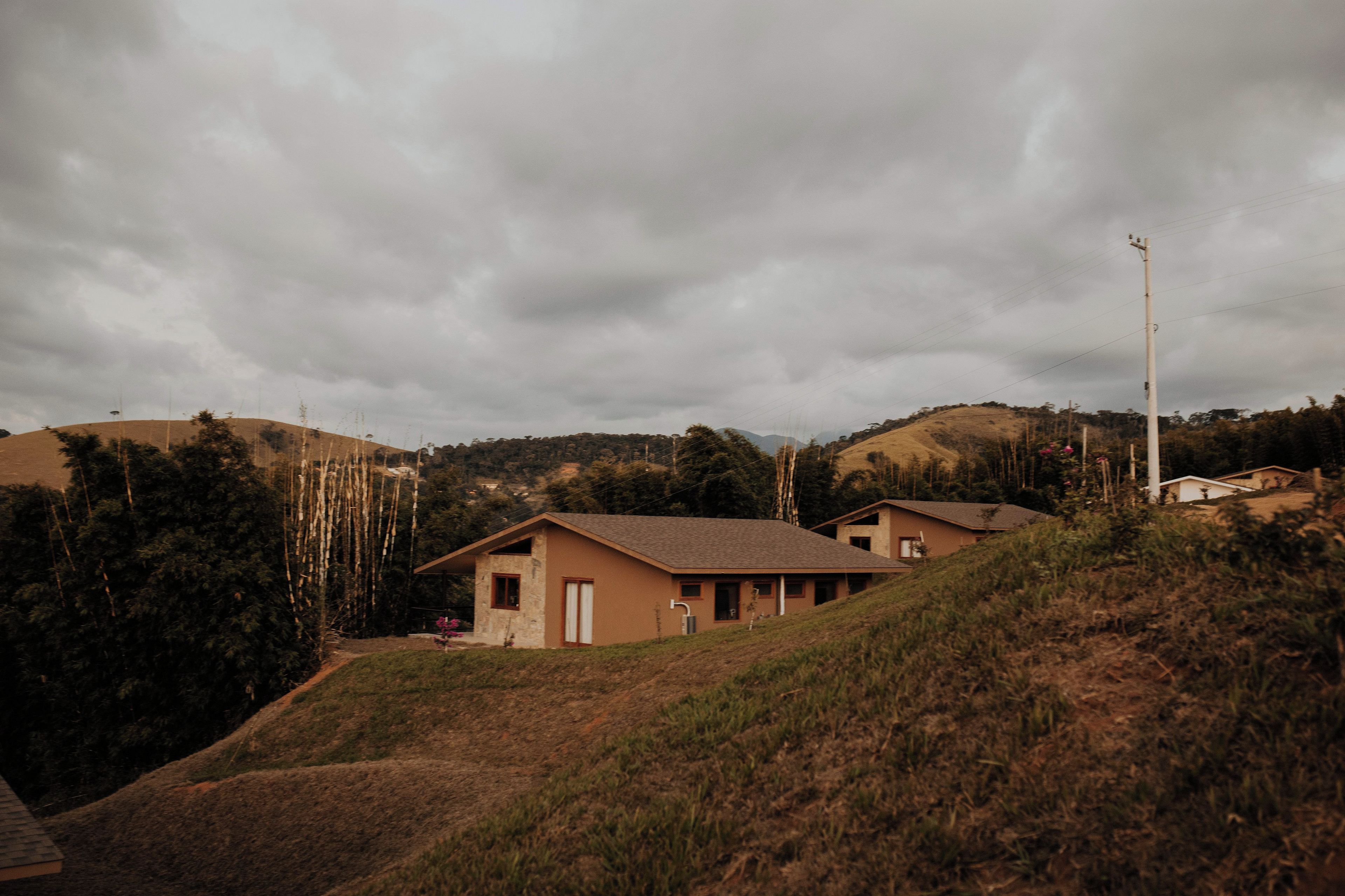 A residential area with houses on a hillside, surrounded by vegetation and under a cloudy sky.