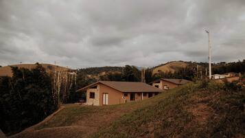 A residential area with houses on a hillside, surrounded by vegetation and under a cloudy sky.