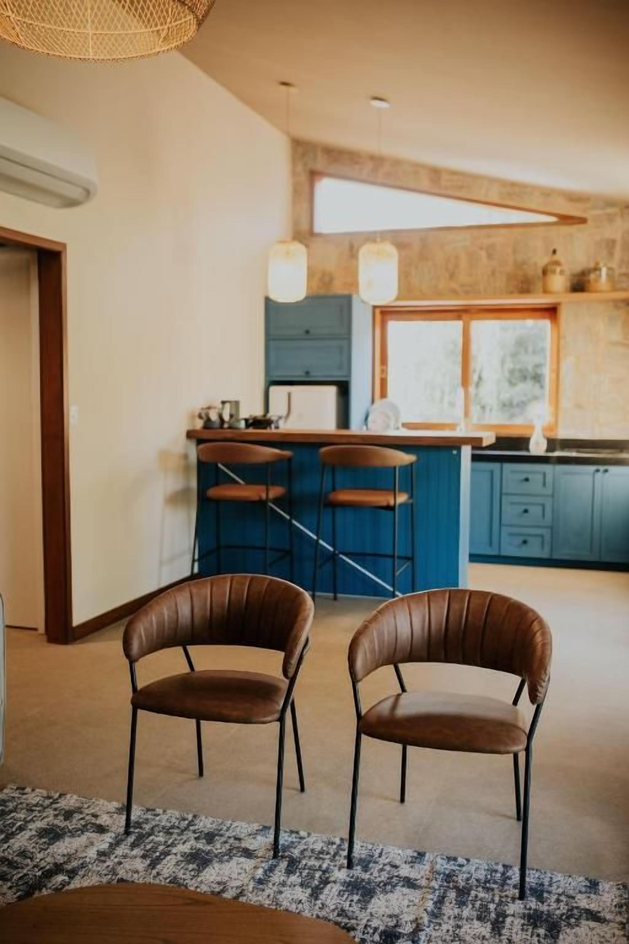 Een moderne keuken met een bar, twee leren stoelen en een groot raam.