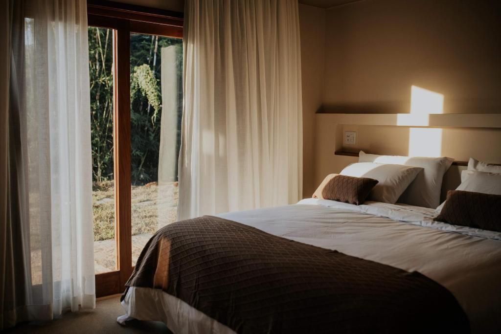 A bedroom with a bed, curtains, and a view of greenery outside.