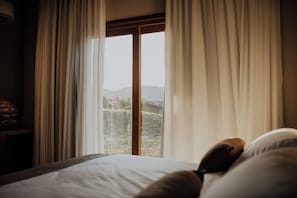 A bedroom with a large window, a bed, and a nightstand with a lamp. - Villa Arouca (Areal)