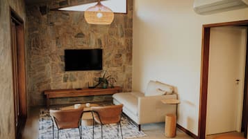 A living room with a stone wall, a flat-screen TV, a sofa, a coffee table, two chairs, a hanging light fixture, and a small side table.