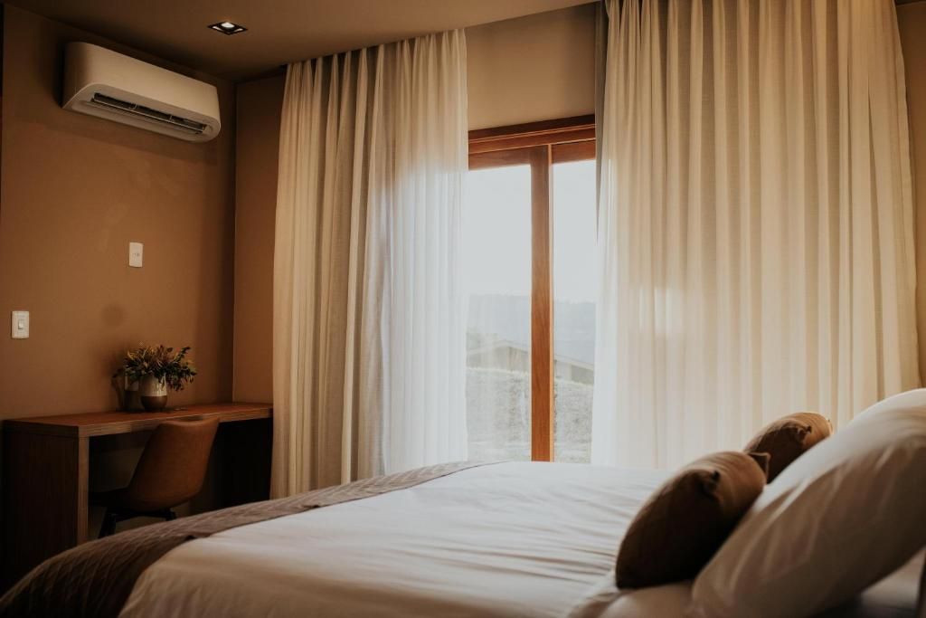 A hotel room with a bed, a desk, and an air conditioning unit.