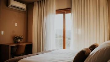 A hotel room with a bed, a desk, and an air conditioning unit.