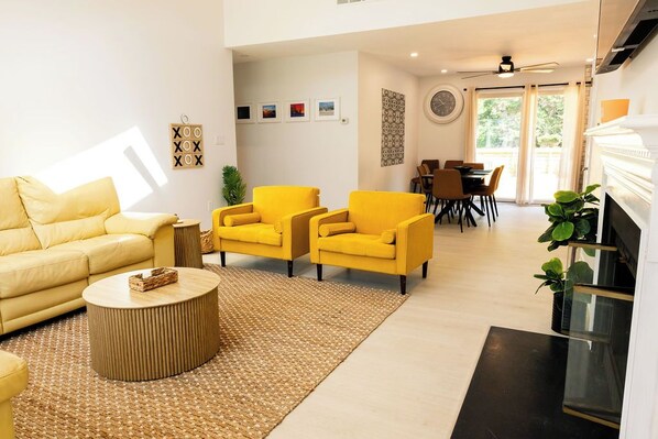 A modern living room with a yellow sofa, two yellow armchairs, a round coffee table, and a fireplace. - 4-bedroom house with larged fenced in yard (Cape May)
