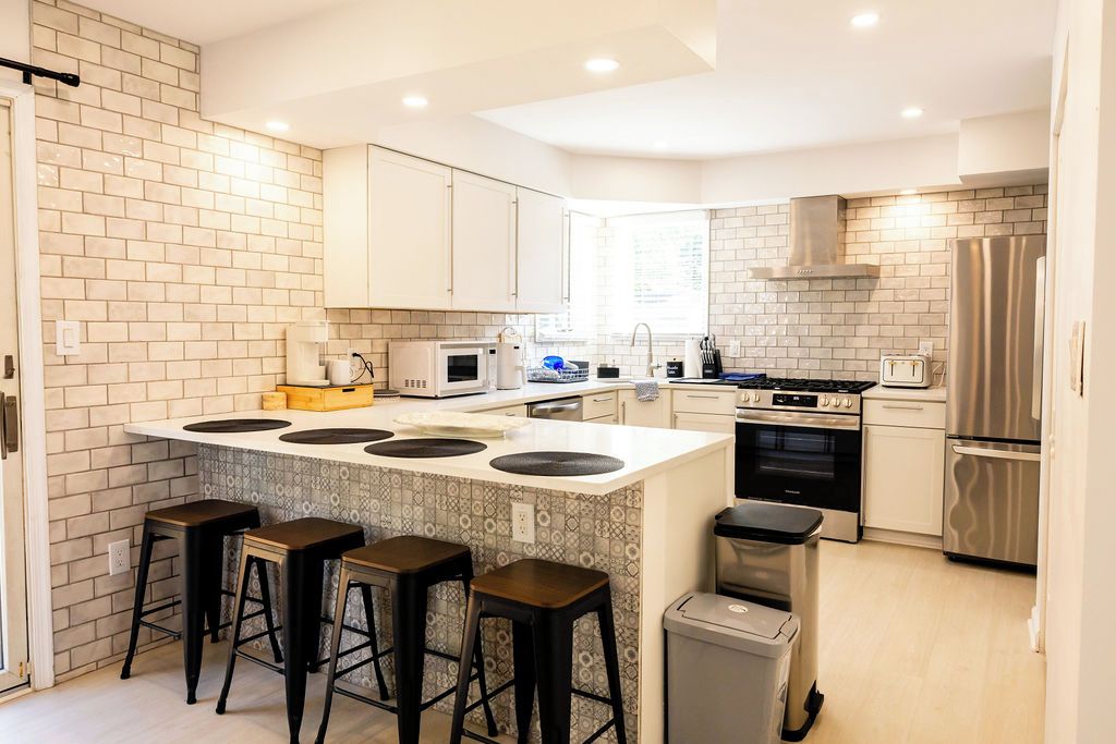 A modern kitchen with a central island, bar stools, stainless steel appliances, and a tiled backsplash.