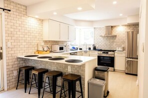 A modern kitchen with a central island, bar stools, stainless steel appliances, and a tiled backsplash.