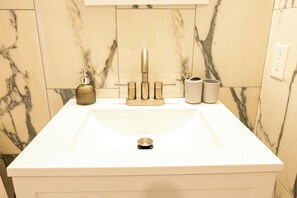A bathroom with a white sink, gold faucet, and marble walls. - 4-bedroom house with larged fenced in yard (Cape May)