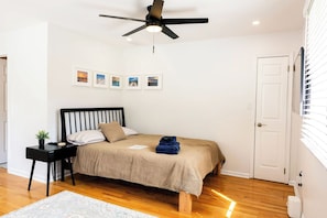 Une chambre à coucher avec un lit, une table de chevet, un ventilateur de plafond et une porte.