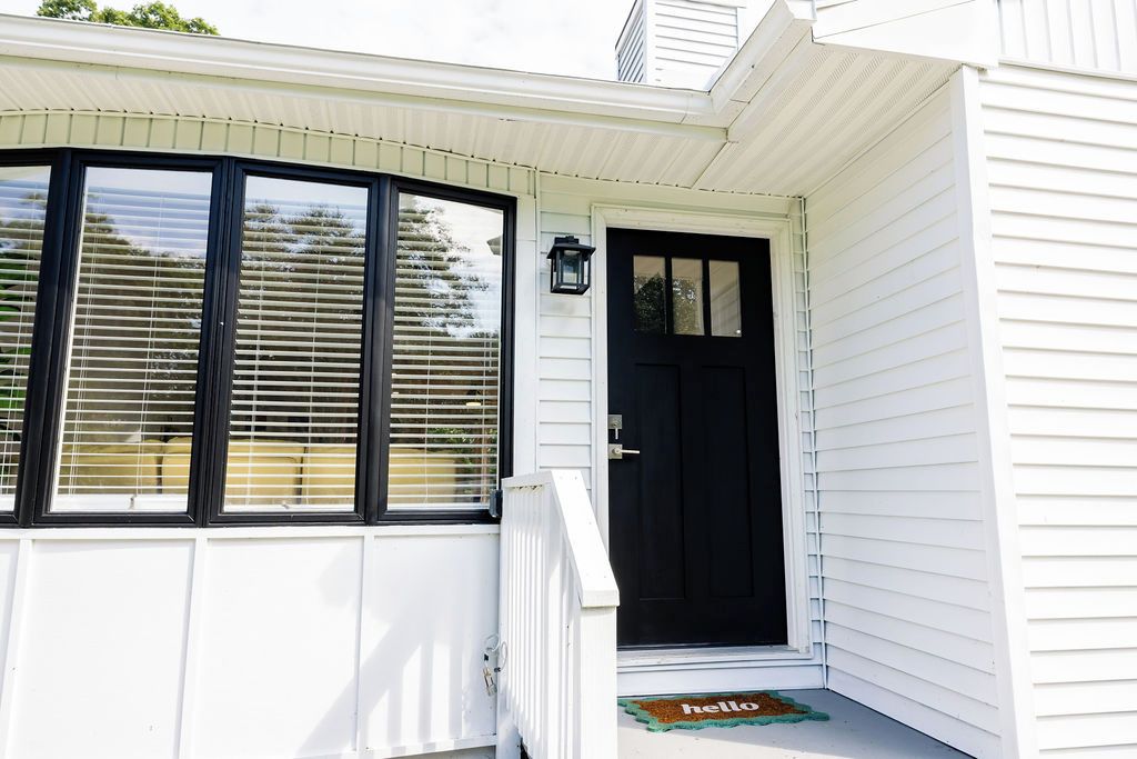 A house with a black front door, a white porch, and a 'hello' mat.