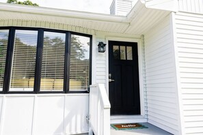 A house with a black front door, a white porch, and a 'hello' mat.