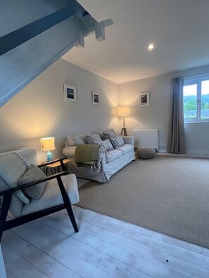 A spacious living room with a high ceiling, a sofa set, a lamp, and a view through a window.