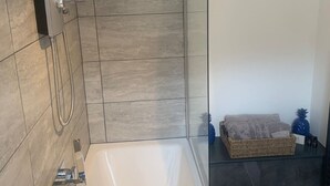 Ein modernes Badezimmer mit einer gläsernen Duschkabine, einer freistehenden Badewanne und einem Korbwannenkorb auf einem Glasregal.