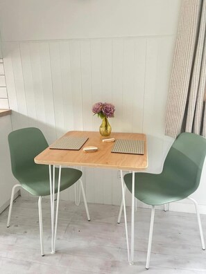 A small dining area with a wooden table, two green chairs, a vase with flowers, and a keyboard on the table.