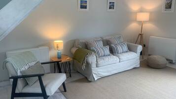 Een gezellige woonkamer met een bank, een fauteuil, een lamp en een radiator.
