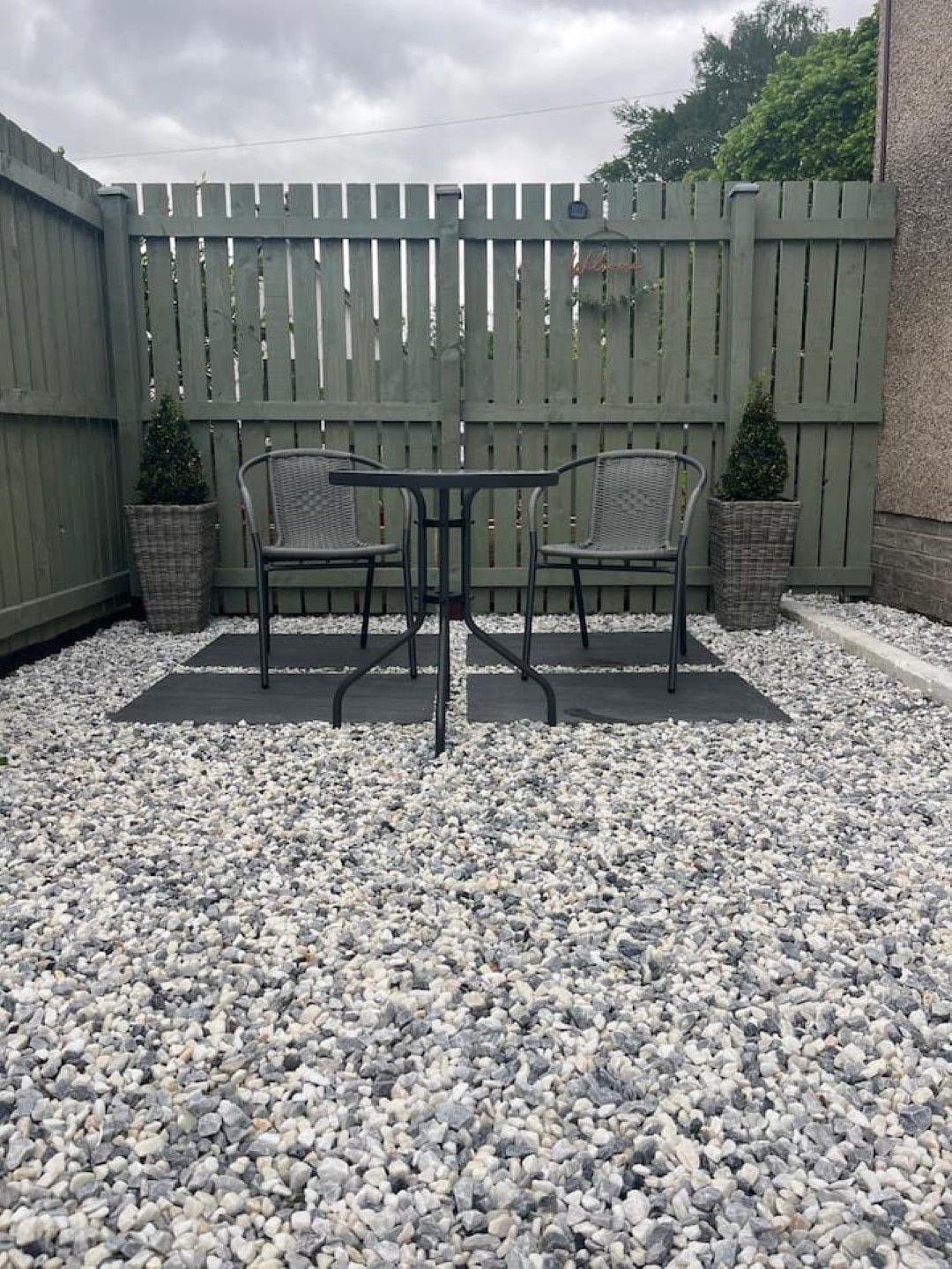 Een terras met twee stoelen en een tafel, omgeven door een houten hek en een grindpad.