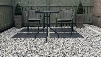 A patio area with two chairs and a table, surrounded by a wooden fence and gravel ground.