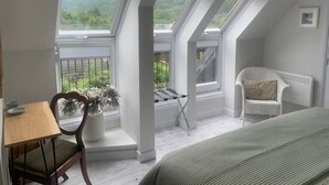 Ein Zimmer mit schrägen Wänden, Blick ins Grüne, ein weißer Stuhl, ein kleiner Tisch und ein Bett.