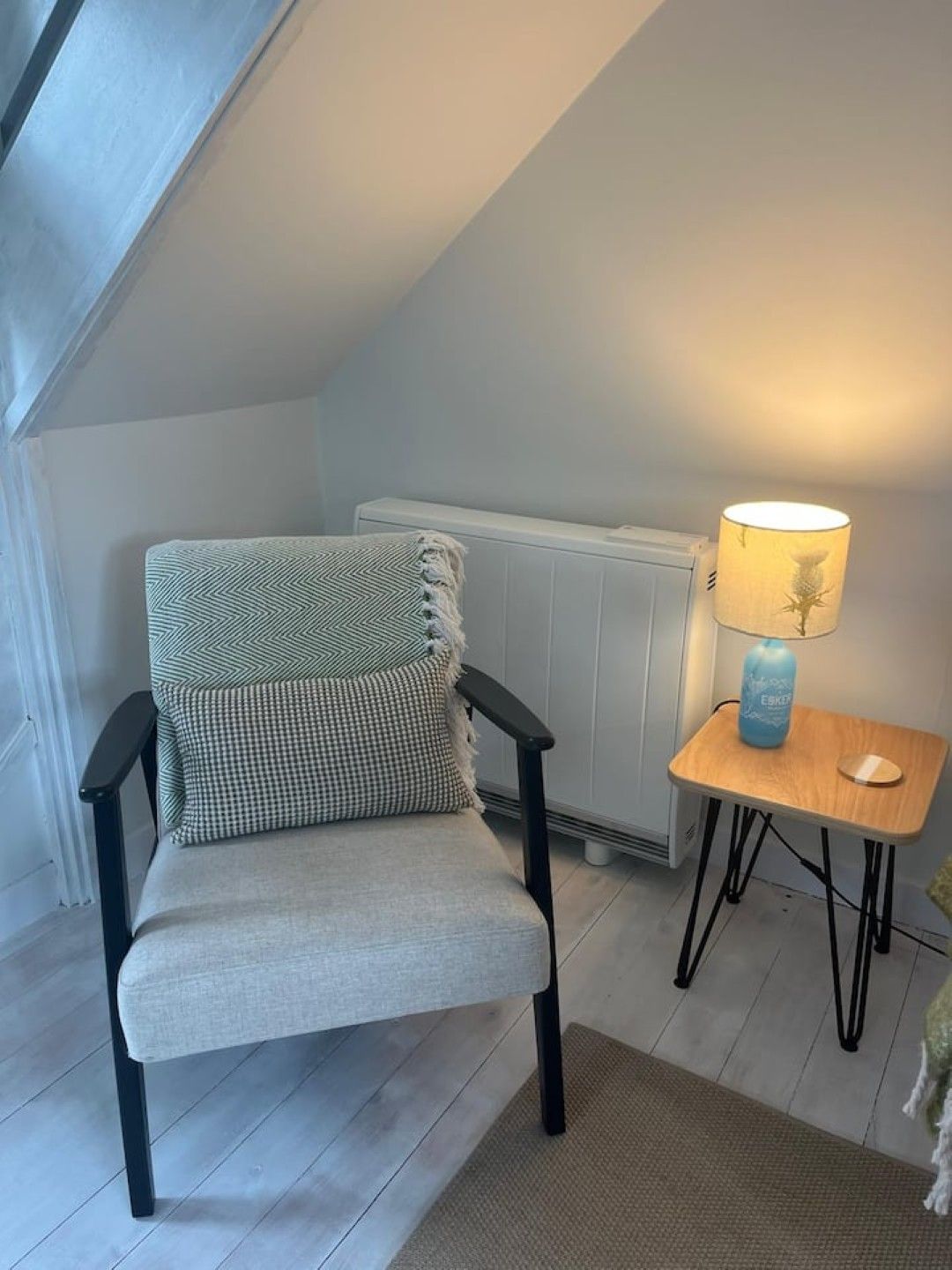 Een stoel met een geruit kussen en een lamp op een klein tafeltje in een kamer met een schuine hemel.