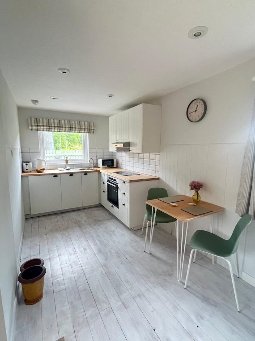 Een kleine keuken met witte kastjes, een magnetron, een spoelbak en een eethoek met twee stoelen.
