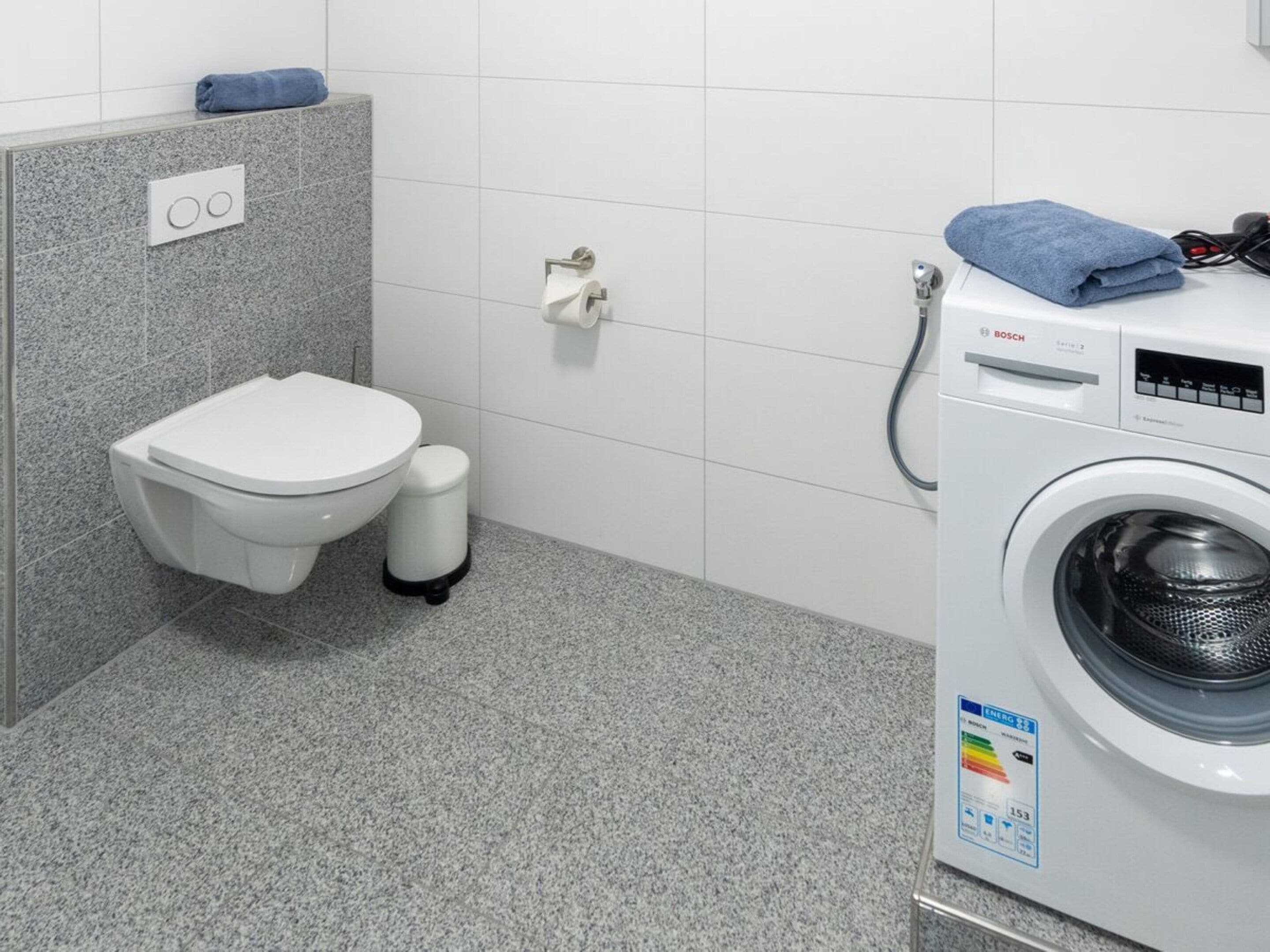 Un baño con inodoro, un cubo de basura y una lavadora.