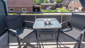 A balcony with two chairs and a table, two cups on the table, and a view of houses in the background. - Holiday Home With 1 Bedroom (Esens)