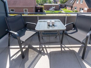 A balcony with two chairs and a table, two cups on the table, and a view of houses in the background. - Holiday Home With 1 Bedroom (Esens)
