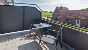 A rooftop terrace with a table and chairs, a metal railing, and a view of a red-brick building. - Holiday Home With 1 Bedroom (Esens)