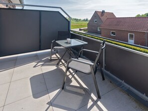 A rooftop terrace with a table and chairs, a metal railing, and a view of a red-brick building. - Holiday Home With 1 Bedroom (Esens)