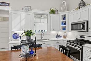A modern kitchen with white cabinetry, a built-in microwave, a stove, and a dining area with a wooden table and chairs.