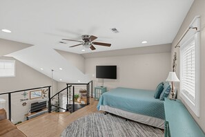 A bedroom with a bed, a ceiling fan, a TV, and a window with blinds.
