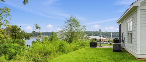 Une cour verdoyante avec un espace patio, un barbecue et une vue sur un lac et des bâtiments éloignés.