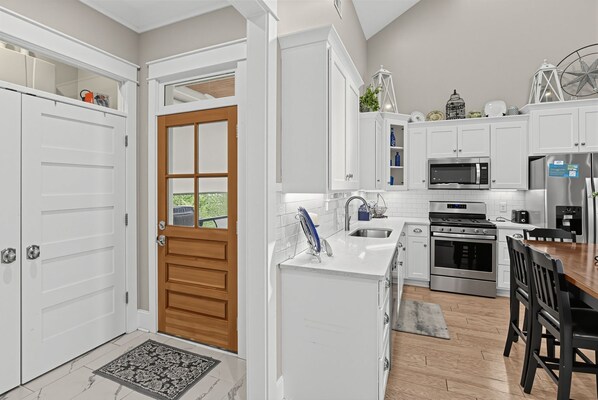 A modern kitchen with white cabinetry, a wooden door, and a dining area with a black table and chairs.