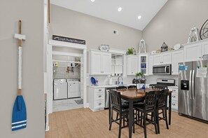 A modern kitchen with white cabinetry, a dining table with chairs, a stainless steel refrigerator, and a microwave.