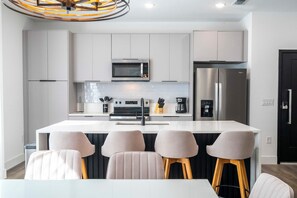 A modern kitchen with a central island, stainless steel appliances, and bar stools. - Modern 4BR Home • Private Pool • Near Disney (Kissimmee)
