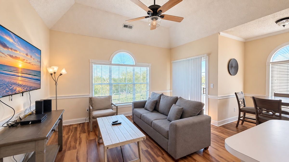 A spacious living room with a sofa, coffee table, and a TV mounted on the wall.